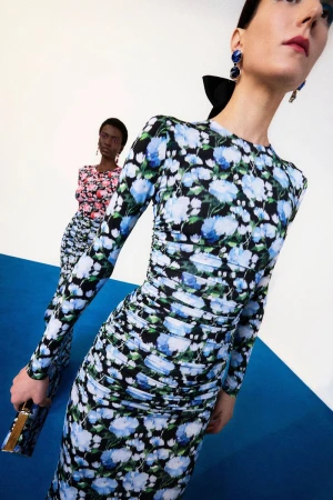 Two models wearing floral dresses in a bright studio with a blue floor for Carolina Herrera Pre-Fall 2025