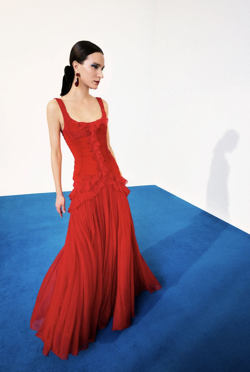 Elegant woman poses in a vibrant red dress, complemented by matching earrings, against a backdrop of white and blue color blocking.