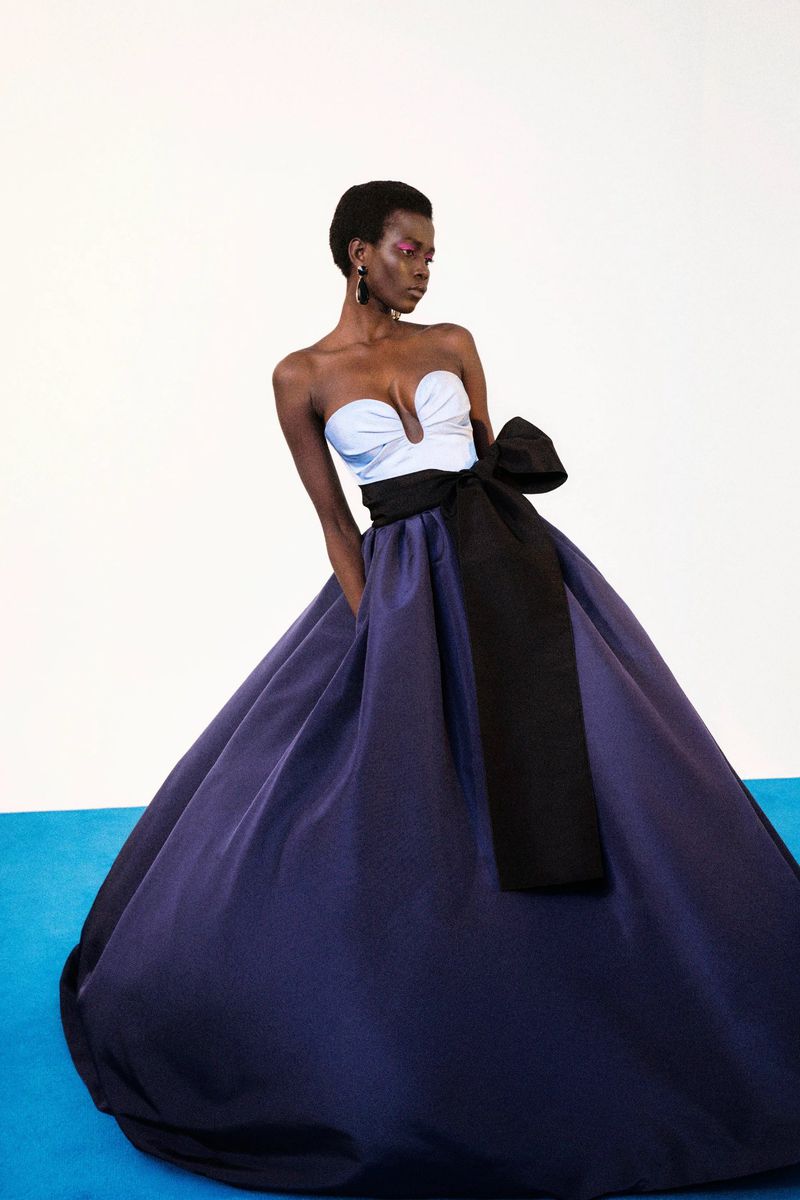 Elegant woman in a strapless blue and black gown with a large bow, posing against a white background with a turquoise accent.