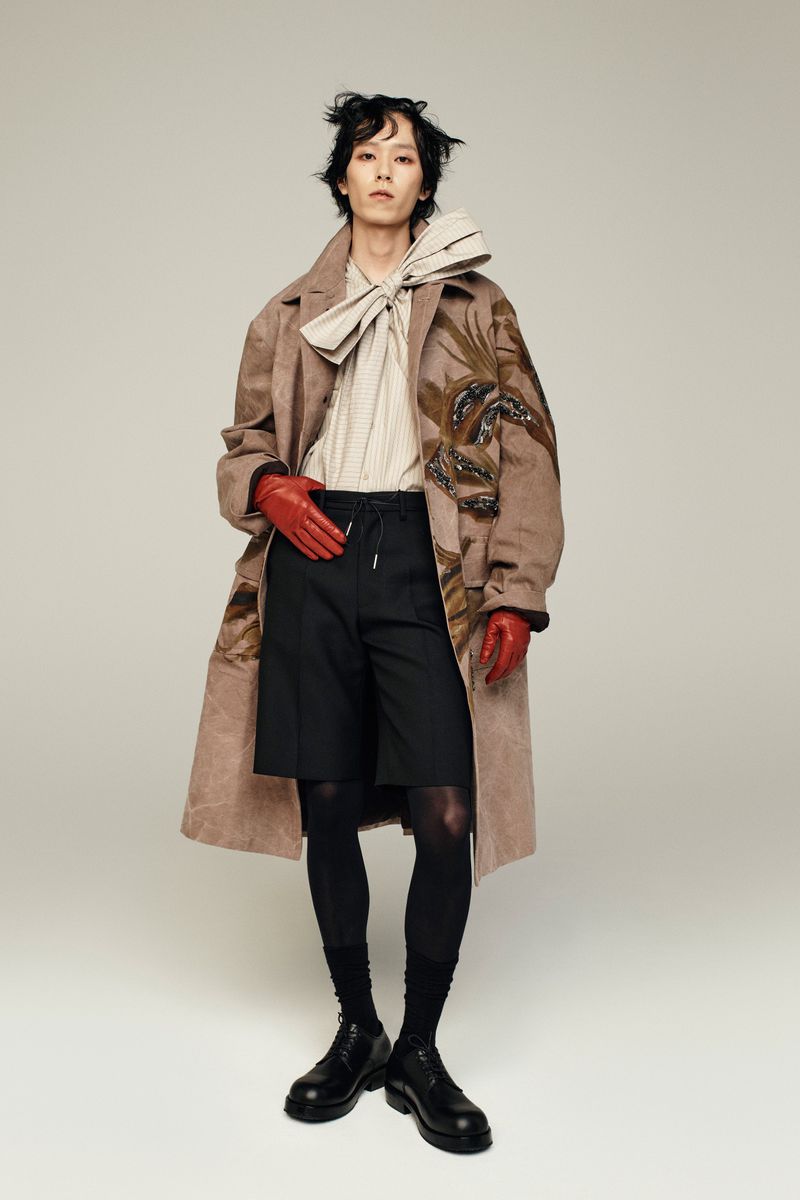 Full-length shot of a fashion model in coat, shorts, tights and gloves posing in a studio. Neutral background.