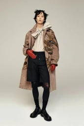 Model in brown patterned coat with red leather gloves against a grey seamless background