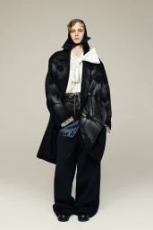 Model in black coat with oversized white bow collar and hood against neutral backdrop for Dries Van Noten