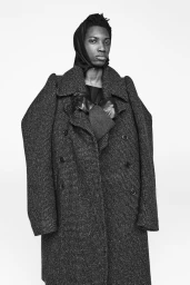Model in textured grey double-breasted coat wearing a headscarf against a plain white background