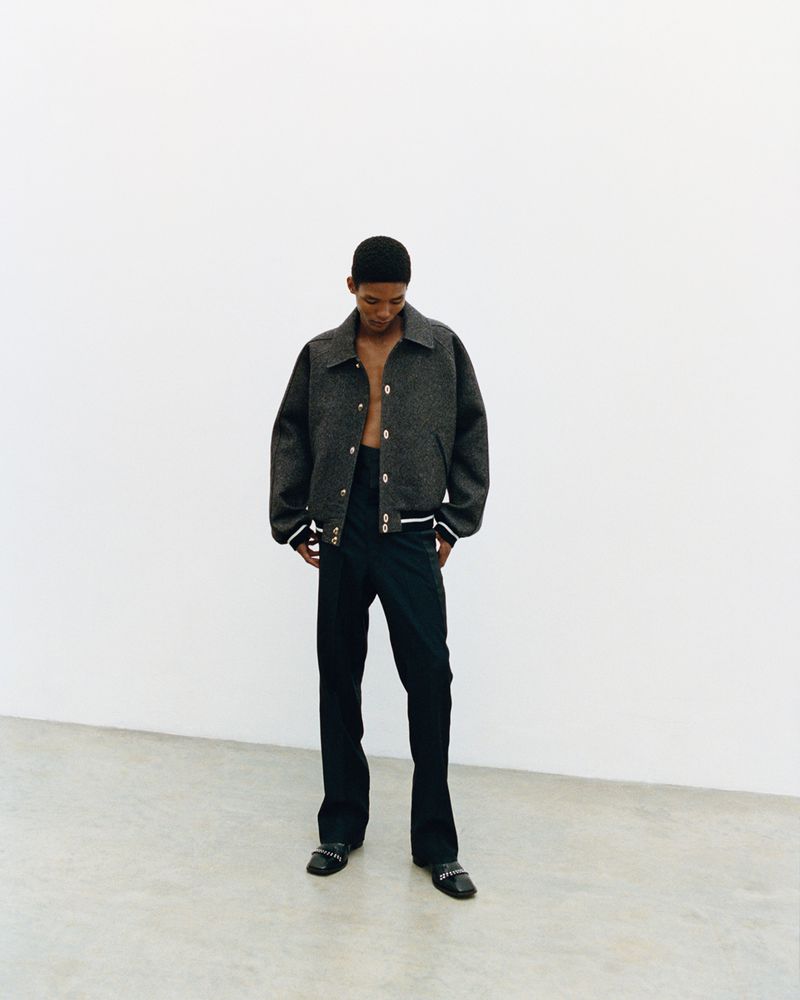 Model wearing a dark textured jacket and trousers against a plain white studio backdrop.