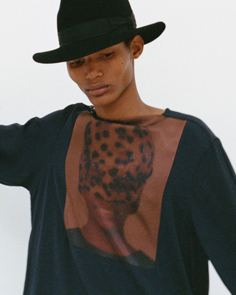 Person wearing a black hat and a navy long-sleeved shirt with a brown and black leopard print graphic on the front against a white background.