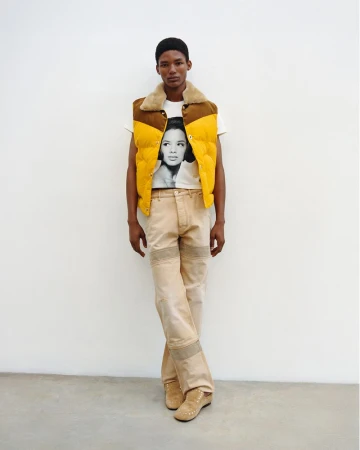 Model Lebo Malope wearing a yellow puffer vest and graphic t-shirt against a white background for Wales Bonner