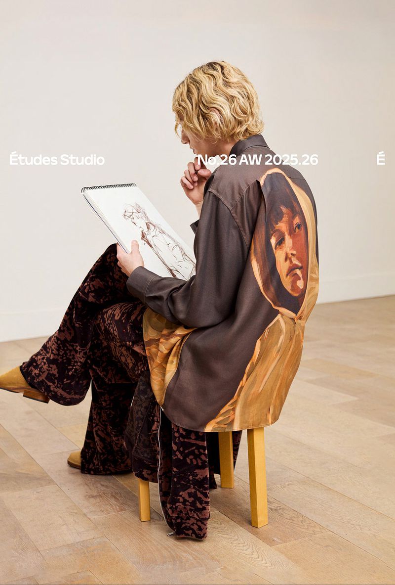 Fashion image: Adult with blond hair sits on a stool drawing. The person wears brown velvet pants and a brown shirt with an image on the back.
