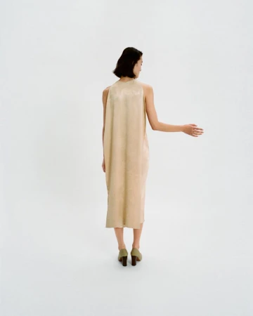 Back view of woman in tan midi dress and green block heel shoes in a minimalist white setting. Fashion shoot, clean style.