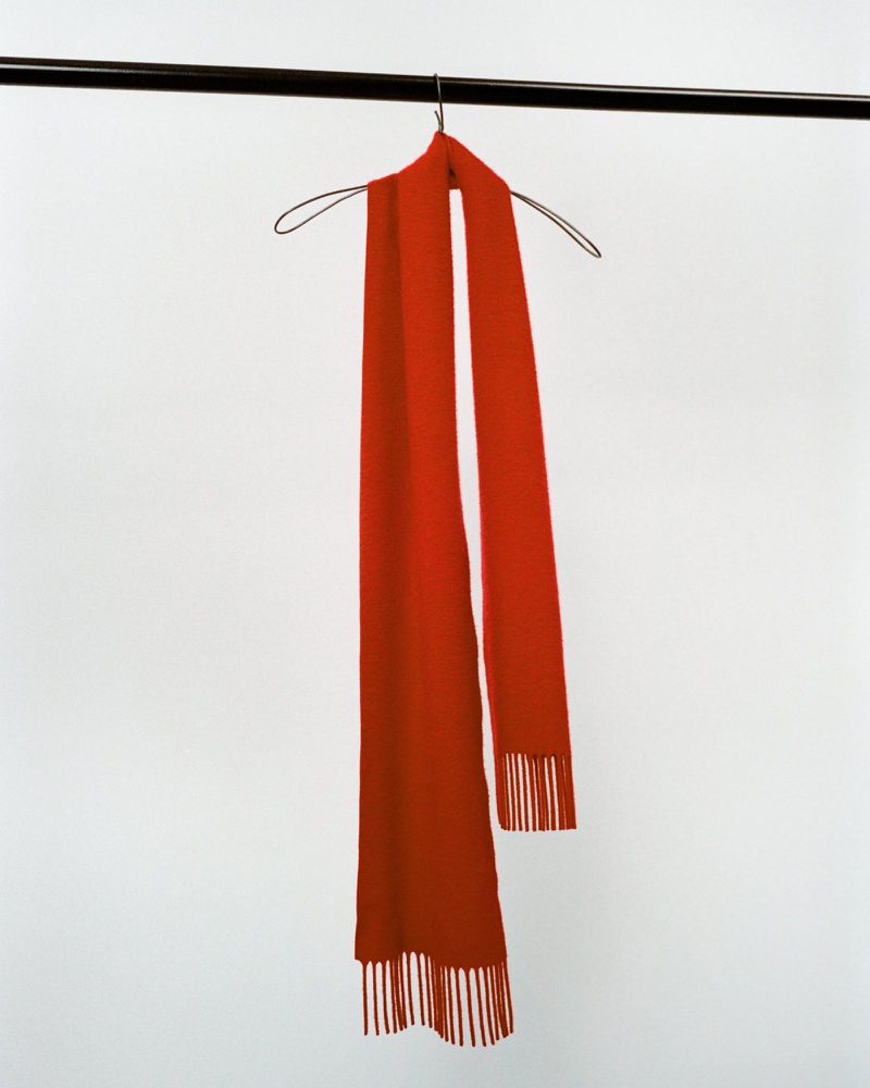 Red scarf hanging on a metal hanger against a white backdrop, showcasing minimalist fashion photography with clean lines and solid colors.