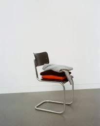 Folded garments stacked on a chrome cantilever chair against a plain background