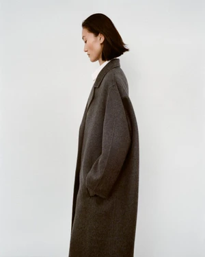 Model Lina Zhang in a dark grey wool coat against a plain white studio background for The Row Fall 2025 campaign.