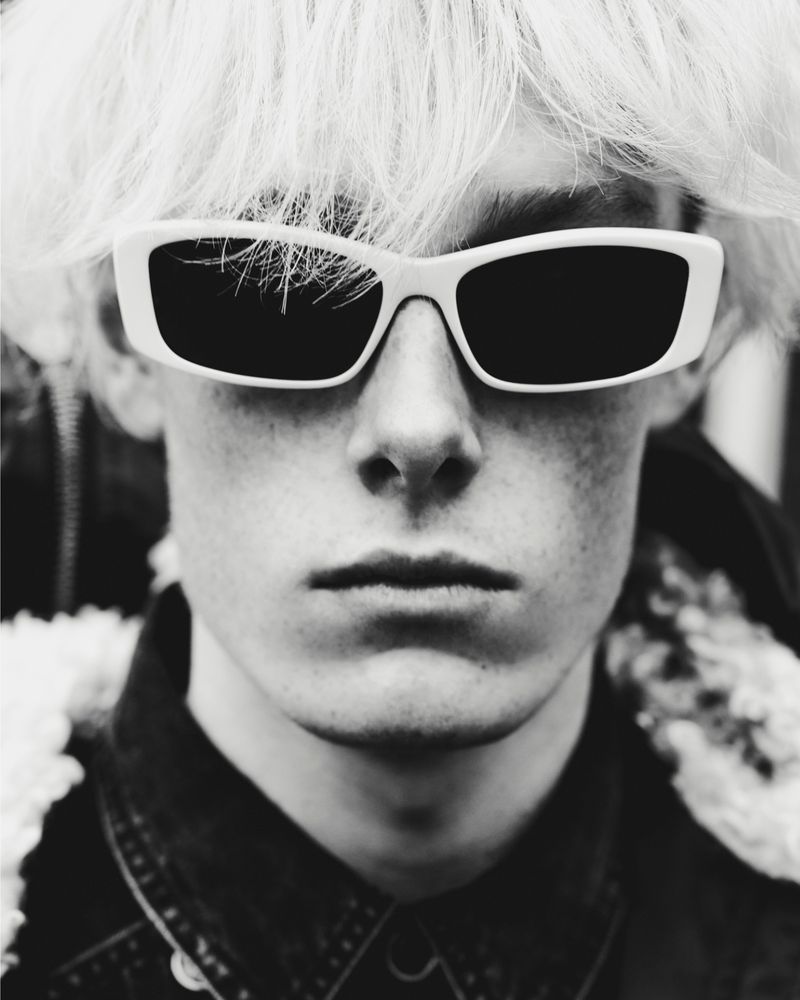 Close-up portrait of a young man wearing white-framed sunglasses and a dark collared shirt for Isabel Marant.