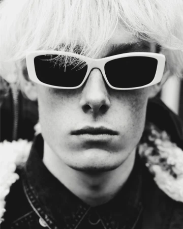 Close-up portrait of a young man wearing white-framed sunglasses and a dark collared shirt for Isabel Marant.