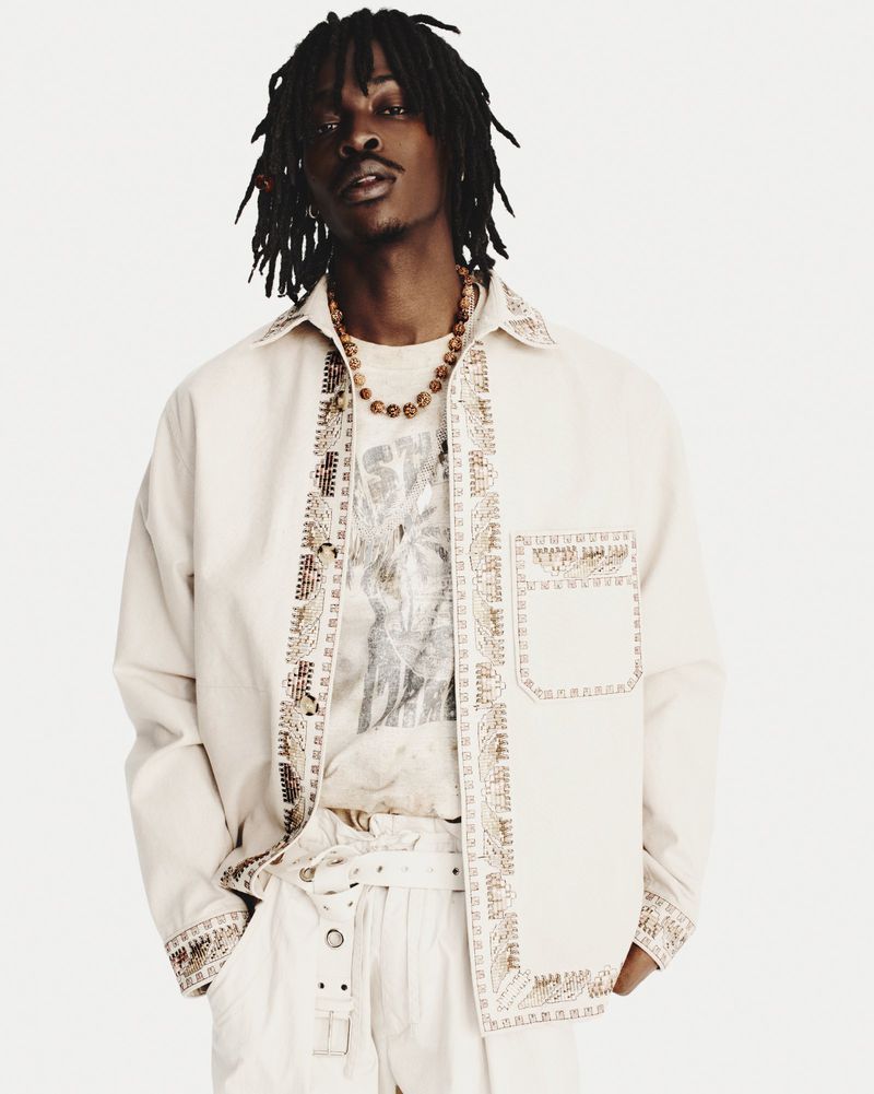 Fashionable black male model wearing a patterned shirt and pants in a bright studio, striking a confident pose for a fashion editorial.