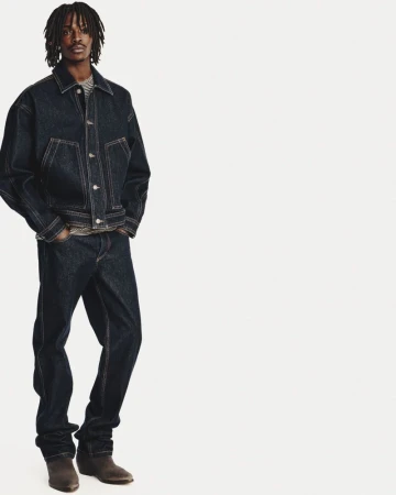 Full-length portrait of a male model wearing a dark denim jacket and matching jeans against a white background.