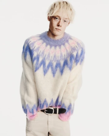 Blonde male model wearing a fluffy Fair Isle sweater with blue and pink patterns and light trousers against a white background