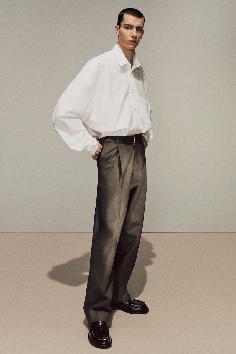 Model wearing a baggy white shirt and grey trousers against a neutral background for Acne Studios fall/winter 2025 menswear lookbook
