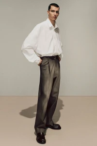 Model wearing a baggy white shirt and grey trousers against a neutral background for Acne Studios fall/winter 2025 menswear lookbook