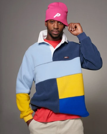 Young adult male in colorful rugby shirt and pink beanie poses in photo studio with neutral gray backdrop; fashion, style, apparel.