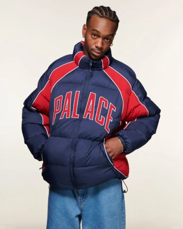 Man wearing a navy and red puffer jacket with blue denim jeans against a seamless white background.