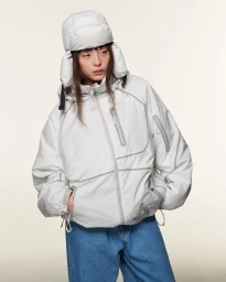 Model wearing a light grey puffer jacket and matching ushanka hat with blue jeans against a neutral studio backdrop