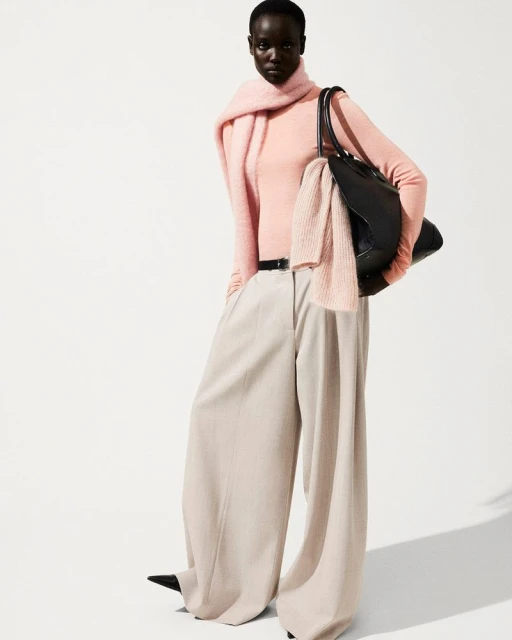 Fashionable dark-skinned woman in a peach top, beige wide-leg pants, and a black tote bag, complemented by a light peach scarf.