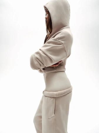 Profile view of a woman wearing a beige hoodie and matching sweatpants against a plain white background.