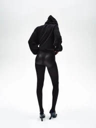 Model from behind wearing a black hoodie and black tights against a white studio background