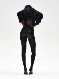 Model with long dark braided hair wearing a black hooded top and leggings against a white background