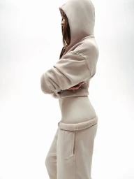 Profile view of a woman wearing a beige hoodie and matching sweatpants against a plain white background.