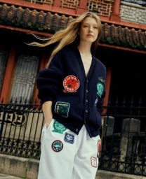 Model with long blonde hair wearing a navy cardigan and white pants decorated with embroidered patches.