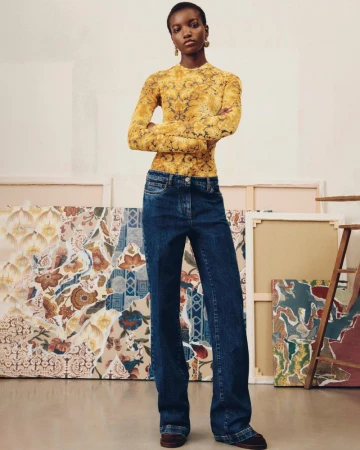 Woman in patterned top and dark denim wide-leg jeans posing in a studio with painted canvas backdrops, fashion editorial shoot.