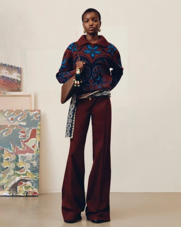 Full-length shot of an African-American woman wearing a patterned sweater, flared pants, and a shoulder bag in a studio setting.