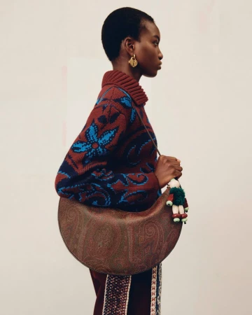 Model in patterned sweater wearing a brown paisley handbag against a neutral studio background