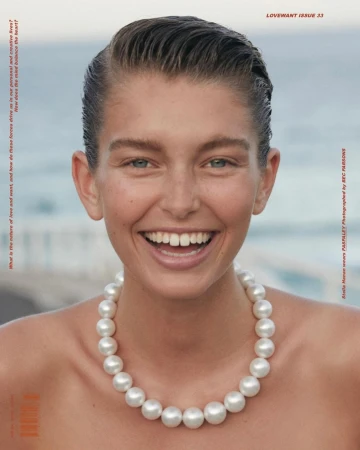Close-up shot of a smiling adult woman with short hair and a pearl necklace, photographed outdoors near the ocean for a magazine cover.