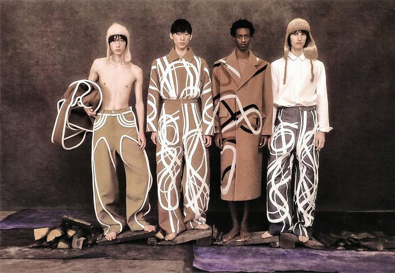 Four slender Asian and Black male fashion models strike a pose against a textured brown backdrop, showcasing unique patterned outfits.