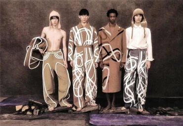 Four male models standing in a line wearing brown and patterned apparel against a dark textured studio backdrop.