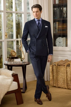 Man in a double-breasted navy pinstripe suit standing in a classic study with a bookshelf and large multi-pane windows.
