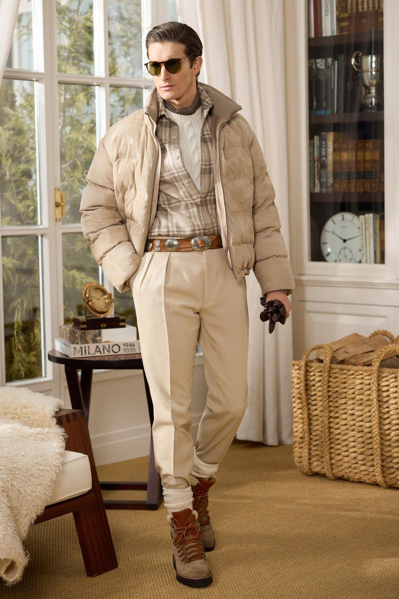 Male fashion model in tan puffer jacket and khaki trousers poses indoors with natural light and classic interior decor.