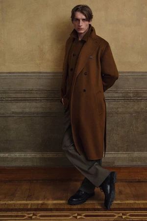 Model wearing a brown double-breasted coat standing against a panelled wall for Brioni F/W 25 Men's Lookbook