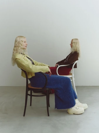 Two blonde models seated on chairs against a plain white studio wall for NIKO and SS25 lookbook photography by Masaya Tanaka.