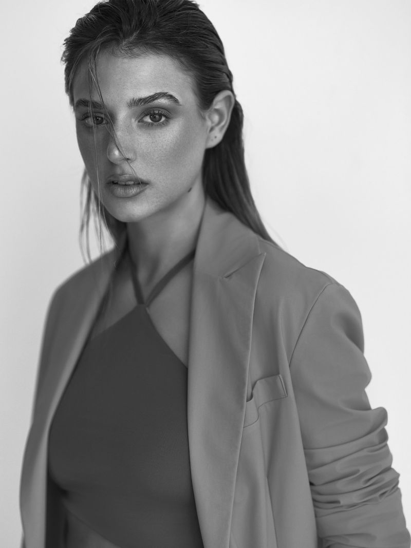 Portrait of a female model with slicked hair wearing a tailored blazer against a plain white seamless studio background.