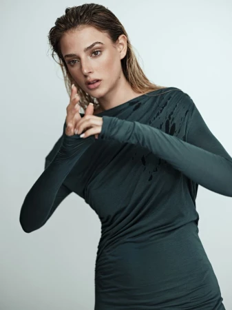 Model with wet hair wearing a dark green long-sleeve top against a light grey studio background.