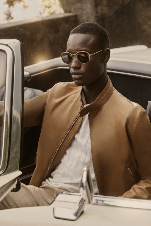 Portrait of an African American man in sunglasses and a tan jacket, seated in a vintage convertible car on an outdoor location.