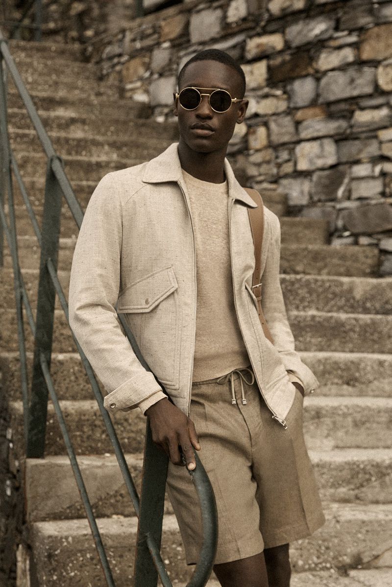 Black man wearing sunglasses and a beige jacket leaning on stone stairs for Brett Johnson