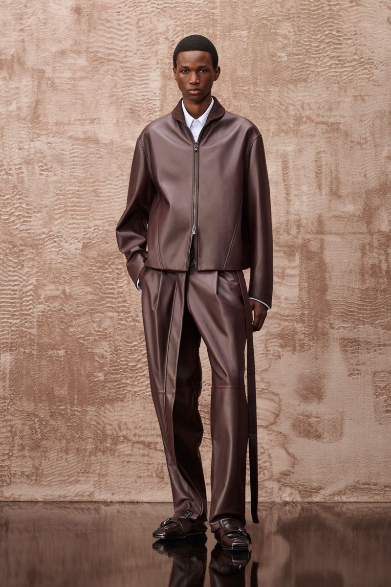 Model in brown leather jacket and matching trousers against textured wall for Ferrari