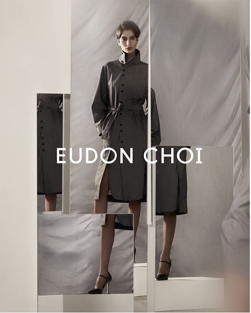 Fashion image features a woman in a grey belted shirt dress and black heels, partially obscured by geometric glass panels in studio.