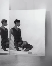 Monochrome portrait of a model crouched on a block, reflected in a large mirror for Eudon Choi Prefall 2025.