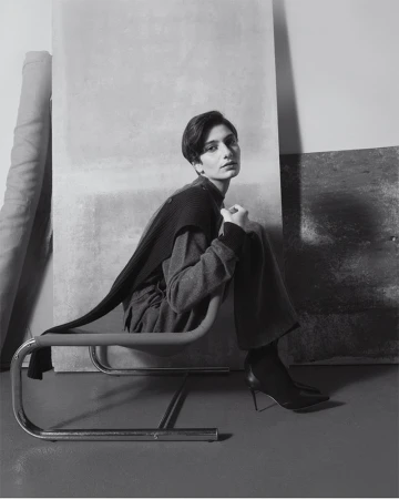 Model seated on a tubular steel chair against layered studio panels in Eudon Choi Prefall 2025 editorial