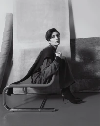 Model seated on a tubular steel chair against layered studio panels in Eudon Choi Prefall 2025 editorial
